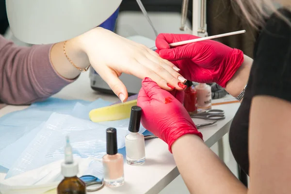 Manicurist with a brush paints nails. Gel polish design. Female master in the salon is painting with brush on the hands of the client. Beauty industry, creativity concept.
