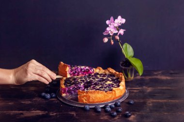 Kadınlar ellerini keser ve bir parça yaban mersinli kırsal ekmek turtası alır. Ve ahşap bir arka planda ekşi krema ve falaenopsis çiçeği ile doludur. Kapat..