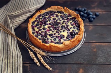 Mutfak havlusu ve buğday kulaklarıyla ahşap zemin dolduran yaban mersinli kır çöreği turtası..