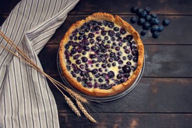 Mutfak havlusu ve buğday kulaklarıyla ahşap zemin dolduran yaban mersinli kır çöreği turtası..