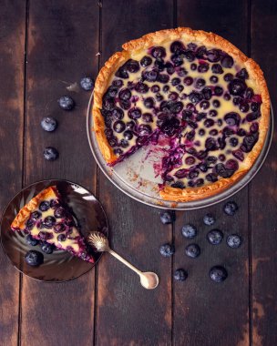 Daire ve kaşıkla kesilmiş bir parça ile ahşap bir zeminde yaban mersinli yaban mersinli börek turtası doluyor. Üst görünüm düzlüğü