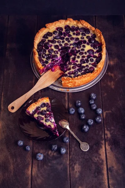 Daire ve kaşıkla kesilmiş bir parça ile ahşap bir zeminde yaban mersinli yaban mersinli börek turtası doluyor. Üst görünüm düzlüğü