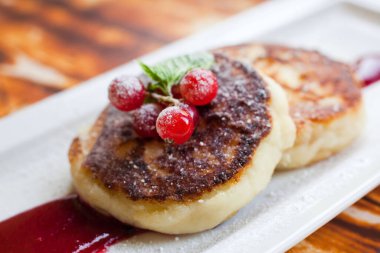 Lezzetli kahvaltı - Frenk üzümleriyle süslenmiş toz şekerle süslenmiş peynirli kekler ve dikdörtgen bir tabakta ekşi kremayla servis edilen reçel