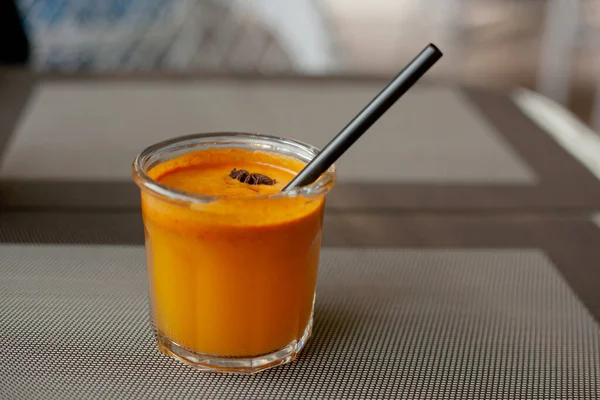 Autumn drink in glass with tube and piece of star anise on the outdoor terrace. Sea-buckthorn smoothie.