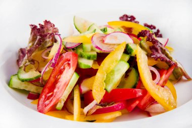 Salatalıklı sebze salatası, domates, turp, turp, dolmalık biber, soğan ve marul. Beyaz bir tabakta yaklaş..