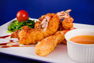 Yağda kızartılmış kaplan karidesleri tatlı ve ekşi sosla servis edilir, Norveç yosunu ve dikdörtgen bir tabakta kiraz domatesleri..