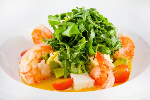 Salad with king prawns, arugula, tomatoes, avocado. Closeup on a white plate.