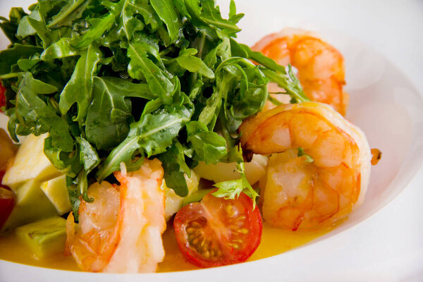 Salad with king prawns, arugula, tomatoes, avocado. Closeup on a white plate.