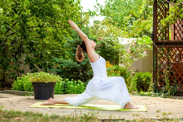 Genç kadın yaz bahçesinde yoga yapıyor - Savaşçı Pozu, Virabhadrasana I.