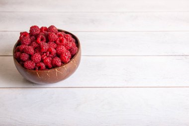 Beyaz ahşap arka planda hindistan cevizi kabuğunda ahududu..