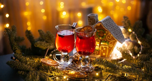 Christmas drink with spicy and berries. Cozy still Life with glasses, gingerbread house and spruce branches.