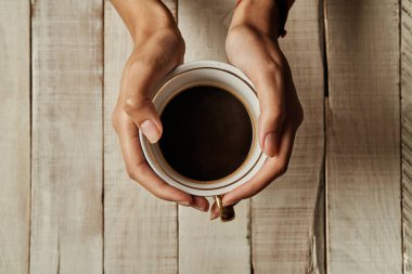 Ahşap bir masanın üzerinde kahve fincanı olan kadın elleri..