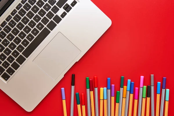 Coloured markers and laptop computer on a red background. Back to school concept, design and creativity.