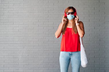 Müzik dinleyen maskeli genç bir kadın. Yeni normallik kavramı ve virüse karşı savaş.