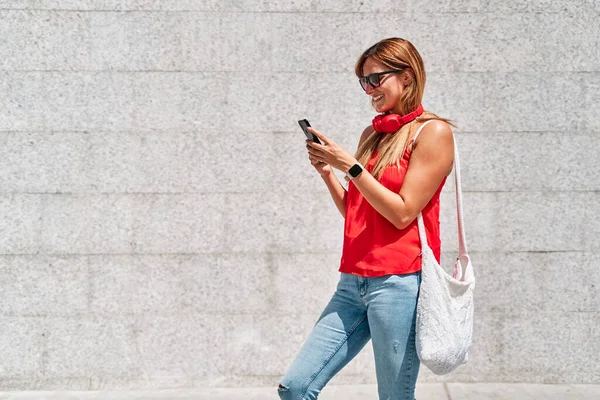 Şehirde cep telefonunu kullanan genç bir kadın. Yeni teknolojiler ve sosyal ağlar kavramı.