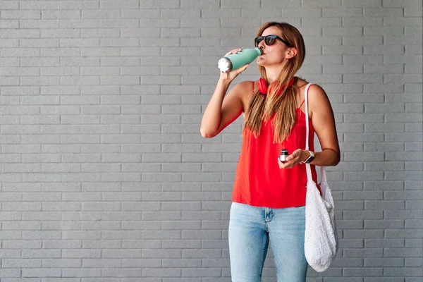 Şişeden su içen genç bir kadın. Sağlıklı yaşam ve iyi alışkanlıklar kavramı.