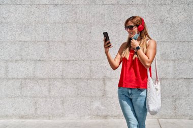 Şehirde cep telefonunu kullanan maskeli genç bir kadın. Yeni normallik kavramı ve virüse karşı savaş.