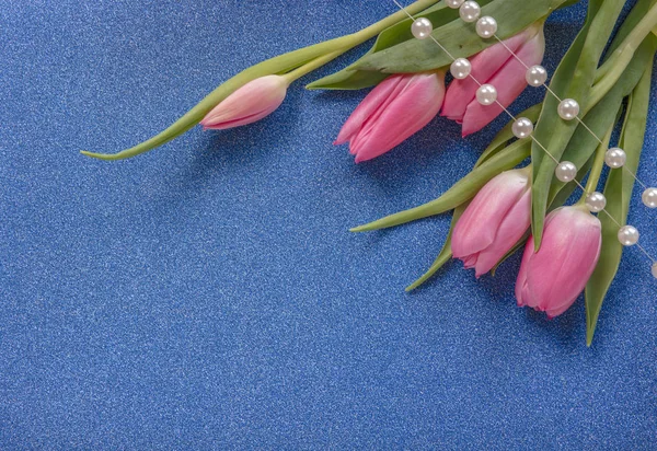 Pink tulips with pearls on blue glitter background with copy space