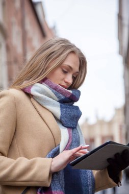 Şehir sokakta tablet tutan sarışın güzel kadın. Bina dışında ayakta tartan eşarp giyen ve tablet kullanarak genç kadının portresi.