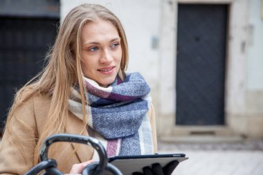 Şehir sokakta tablet tutan sarışın güzel kadın. Bina dışında ayakta tartan eşarp giyen ve tablet kullanarak genç kadının portresi.