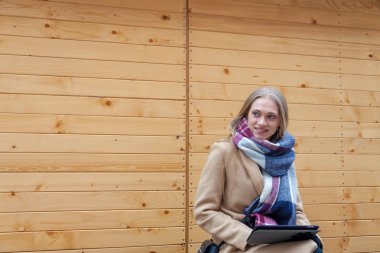 Tablet açık tutan sarışın güzel kadın. Tartan eşarp ahşap duvar önünde ve tablet kullanarak genç kadın portresi. 