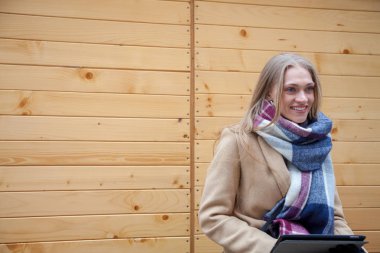 Tablet açık tutan sarışın güzel kadın. Tartan eşarp ahşap duvar önünde ve tablet kullanarak genç kadın portresi. 