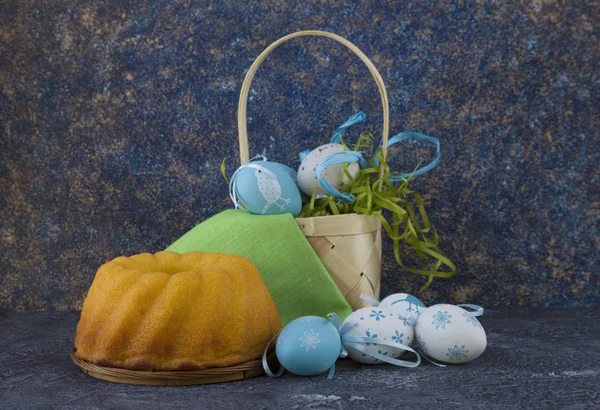 Easter bread and blue Easter eggs in a basket on dark stone table