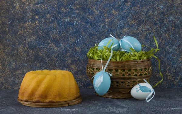 Easter bread and blue Easter eggs in a basket on dark stone table