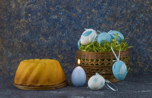Easter bread and blue Easter eggs in a basket on dark stone table