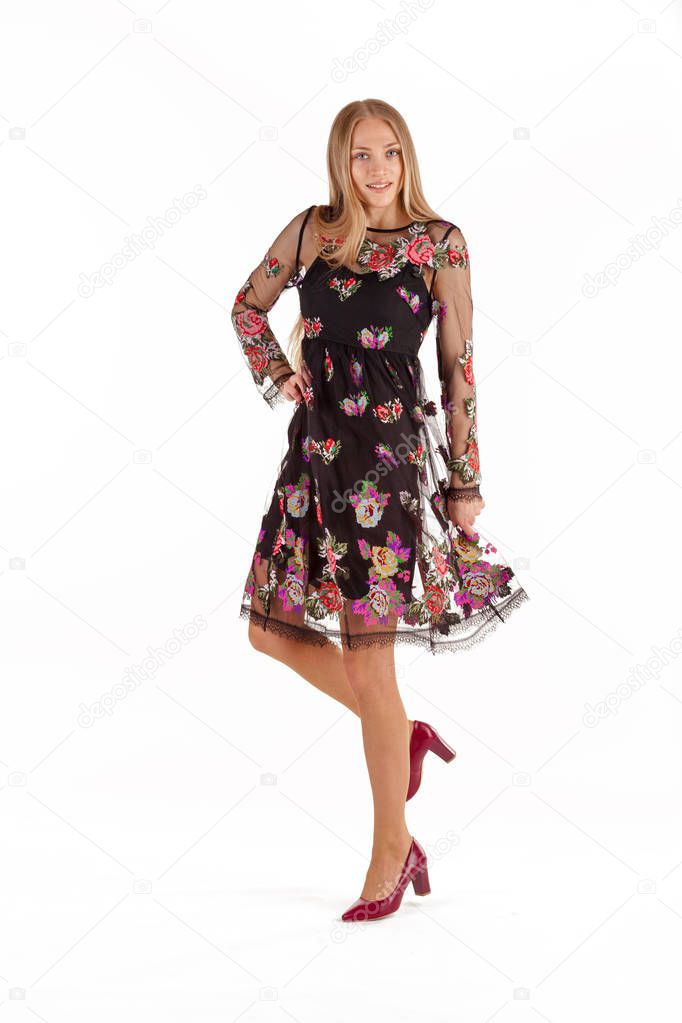 Beautiful young blonde woman in black dress with floral embroidery isolated on white background