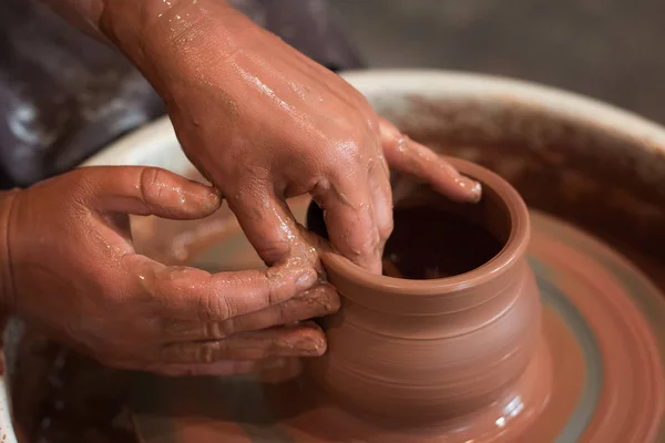 La ruota di vasaio rotante e la merce di argilla su esso presa dall'alto. Uno scolpisce le mani con una coppa di argilla sulla ruota di un vasaio. Mani in argilla . — Foto Stock