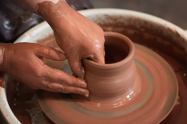 Rotating potter's wheel and clay ware on it taken from above. A sculpts his hands with a clay cup on a potter's wheel. Hands in clay.