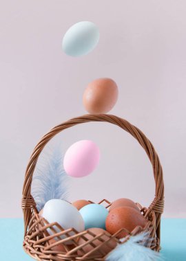 Paskalya kompozisyon. Çok renkli yumurtalar sepete düşüyor. Pembe-mavi bir arka planda. Mutlu Paskalya. 