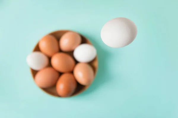 O ovo branco cai em uma chapa de madeira com ovos em uma mesa azul. Feliz Páscoa. Foco seletivo. Vista superior — Fotografia de Stock