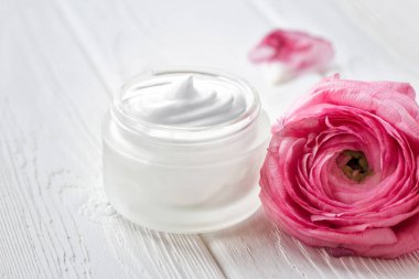 Ahşap bir yüzey üzerinde yüz kremi ve pembe ranunculus çiçek ile Kavanoz. Metin için yer. Yakın çekim. 