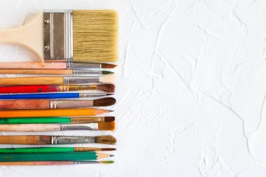 Beyaz doku arka planında farklı boyutlarda boya fırçaları ve kalemler. Sanat ve eğitim nesnesi