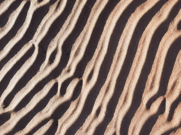 Natural textured sand on sand dunes. Sandy beach in the evening, background with lines on the sand