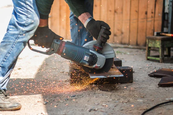 Händerna på människan med stålfräs verktyg. Arbetaren utanför, klipper plåt. Elsåg genererar heta gnistor. — Stockfoto