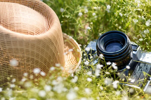 The vintage camera camera and straw hat in a grass in sunny day. Summer holidays and vacation travel concept.