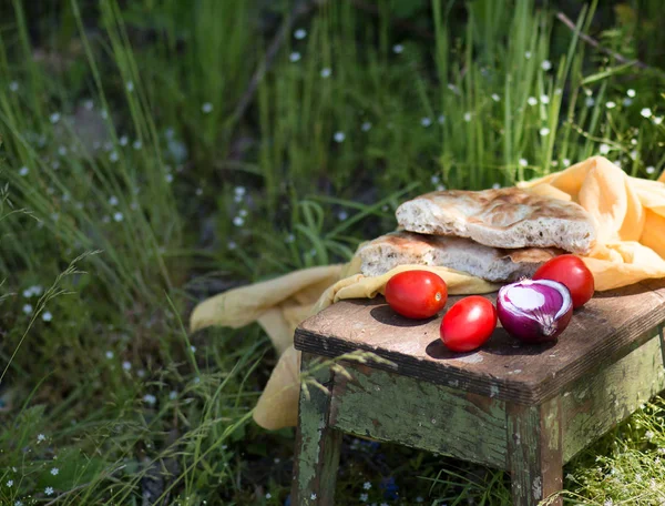 Nourriture campagnarde dans le style de l'agriculteur : le pain cuit au four, oignons, tomates sur un vieux tabouret en bois à l'extérieur dans une journée d'été ensoleillée — Photo