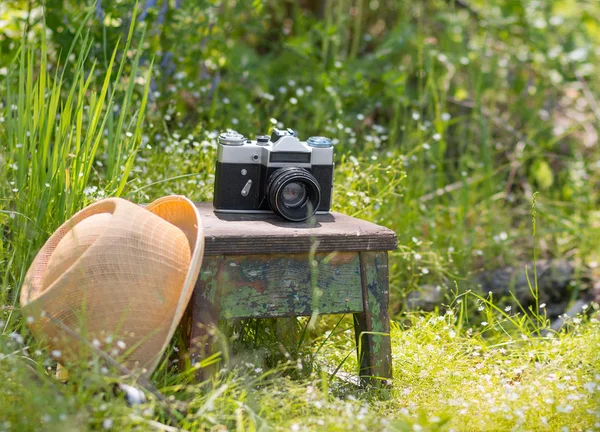 Straw hat and the retro film photo camera on a wooden chair in the summer garden. Vacation, tourist and travel concept — Stock Photo, Image