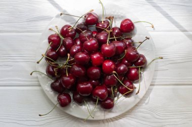 Beyaz ahşap masada beyaz plaka kırmızı tatlı kiraz meyve