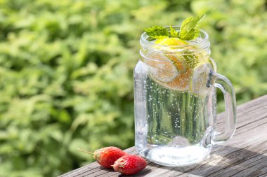 Eski bir ahşap masada bir cam kavanozda limon ve nane ile limonata. Arka planda yeşil çim. Yaz içeceği