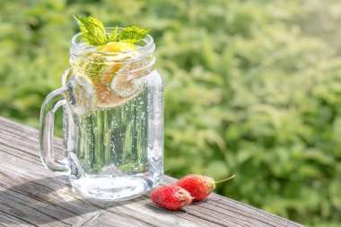 Eski bir ahşap masada bir cam kavanozda limon ve nane ile limonata. Arka planda yeşil çim. Yaz içeceği