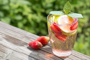 Çilekli limonata, eski ahşap bir masanın üzerindeki cam kavanozda limonata ve nane. Arka planda yeşil çimenler var. Yaz içeceği