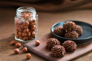 Paslı metal bir yüzey üzerinde siyah bir tabakta trüf çikolatalı mini kek, bir filbert ile banka. Tatlılar ve fındık