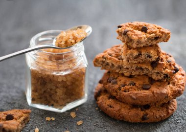 Taze pişmiş çikolatalı kurabiye ve gri bir masada kahverengi şeker ile cam bir kavanoz