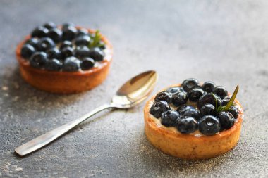 Gri arka plan üzerinde küçük bir kaşık ile vanilyalı muhallebi krem ile Lezzetli yaban mersini tartlets. Ön görünüm. 