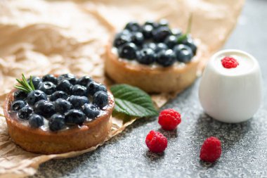 Vanilya kreması ile lezzetli yaban mersini tartalet ve gri bir arka plan üzerinde siyah ve beyaz plaka üzerinde ahududu ile.