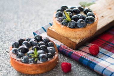 Ahududu taze çilek ile, damalı peçete ile gri masada yaban mersini ile Tartlets. Üstte görüntü